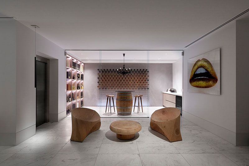 This modern house has a wine cellar that's partitioned by a floor-to-ceiling glass wall. Hidden lighting creates a showroom-like atmosphere, while a couple of sculptural wood chairs provide a quiet place to enjoy a glass of wine. #ModernWineCellar #WineStorage