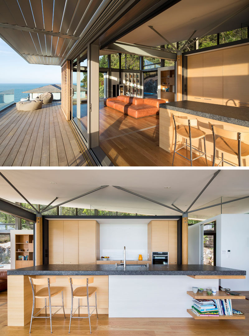 The top level of this modern house has an open plan kitchen, a dining and lounge area, a small study, and a toilet. In the kitchen, wood cabinets are combined with a thick dark countertop for a contemporary appearance. #ModernKitchen #KitchenDesign #OpenPlan