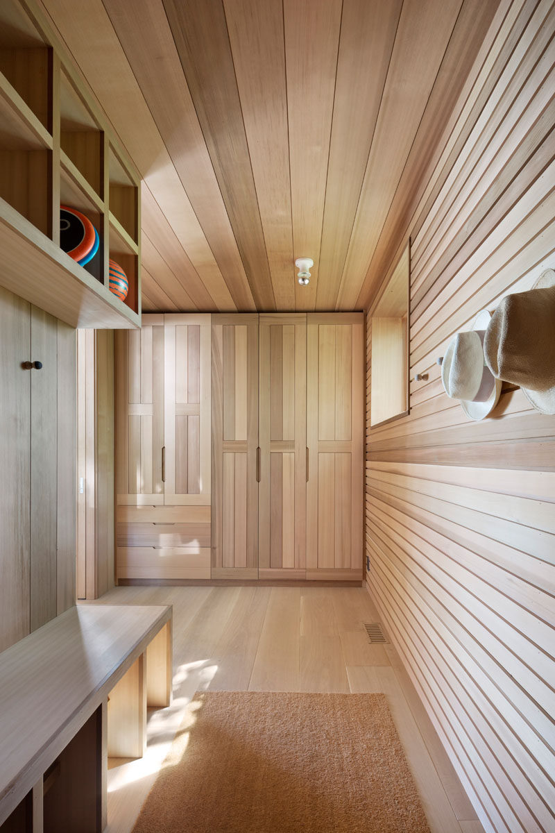 This wood-lined mudroom has floor-to-ceiling cabinets, hooks, and open shelving, providing plenty of space to store coats and shoes. #MudRoom