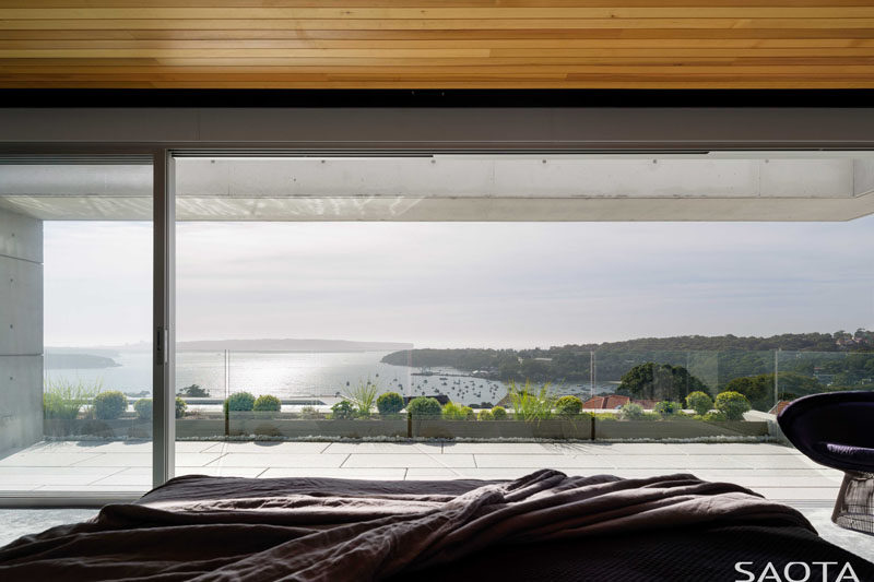 This modern master bedroom, with its wood ceiling, opens up to a balcony with expansive water views. #MasterBedroom #WoodCeiling #Balcony