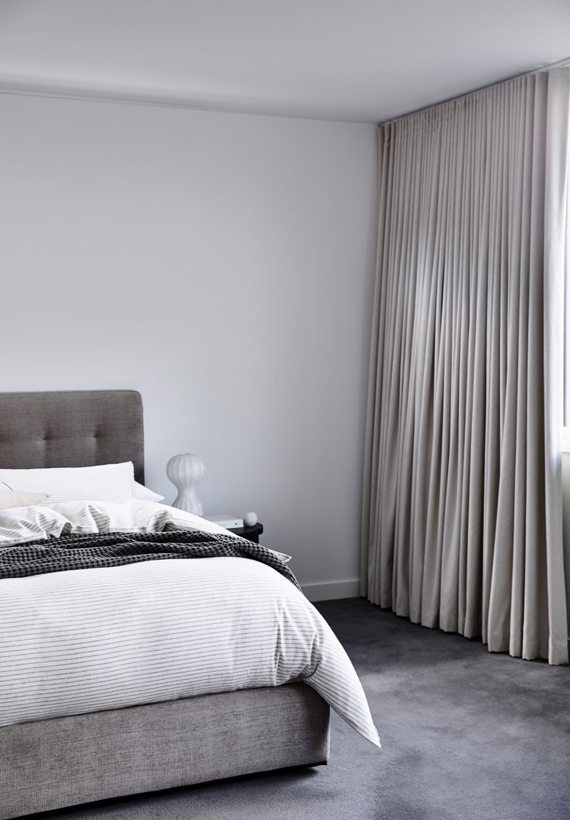 This master bedroom is minimalist in its design, with a grey color palette, and floor to ceiling light curtains to provide privacy. #ModernBedroom #BedroomDesign #MinimalistBedroom