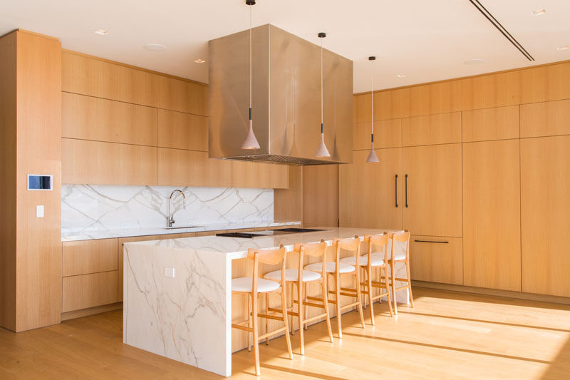 In this modern kitchen, light wood has been used for the cabinets, while the stone island ties in with the countertop and backsplash. #ModernWoodKitchen #KitchenDesign