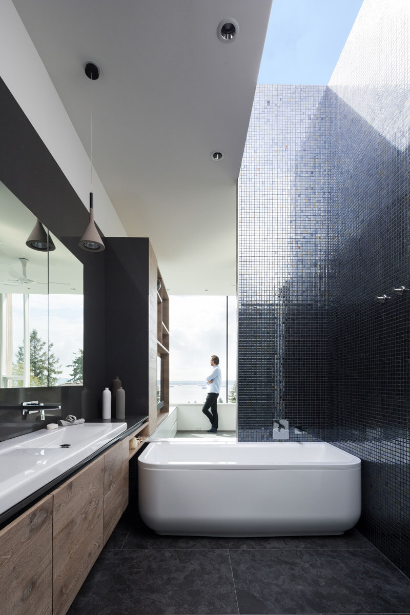 This modern ensuite bathroom has metallic tiles that reflect the natural light from the skylight, and a bathtub that when used, has a view through the bedroom and to the water views in the distance. #ModernBathroom #MetallicTiles #Skylight