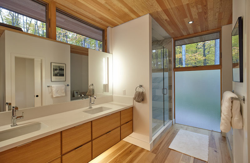 In this contemporary bathroom, a double sink wood vanity with a white countertop sits beside a walk-in shower. A frosted window provides privacy, but at the same time, still lets the natural light through. #BathroomDesign #ContemporaryBathroom #FrostedWindow