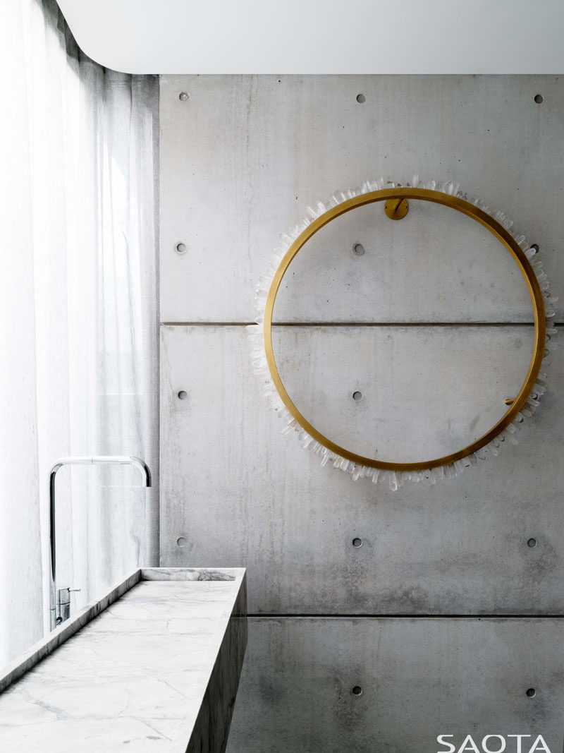 a long stone trough sink is positioned in front of the window that has a billowing curtain. #ConcreteWall #Bathroom #ModernBathroom