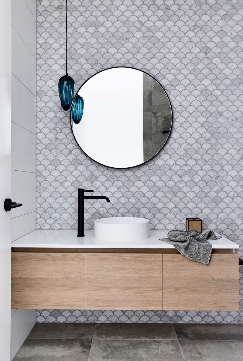 In this modern bathroom, fish scale tiles (also known as scalloped or fan tiles) have been used to create a decorative accent wall, while the blue light fixture adds a pop of color. #ModernBathroom #FishScaleTiles #ScallopTiles #FanTiles