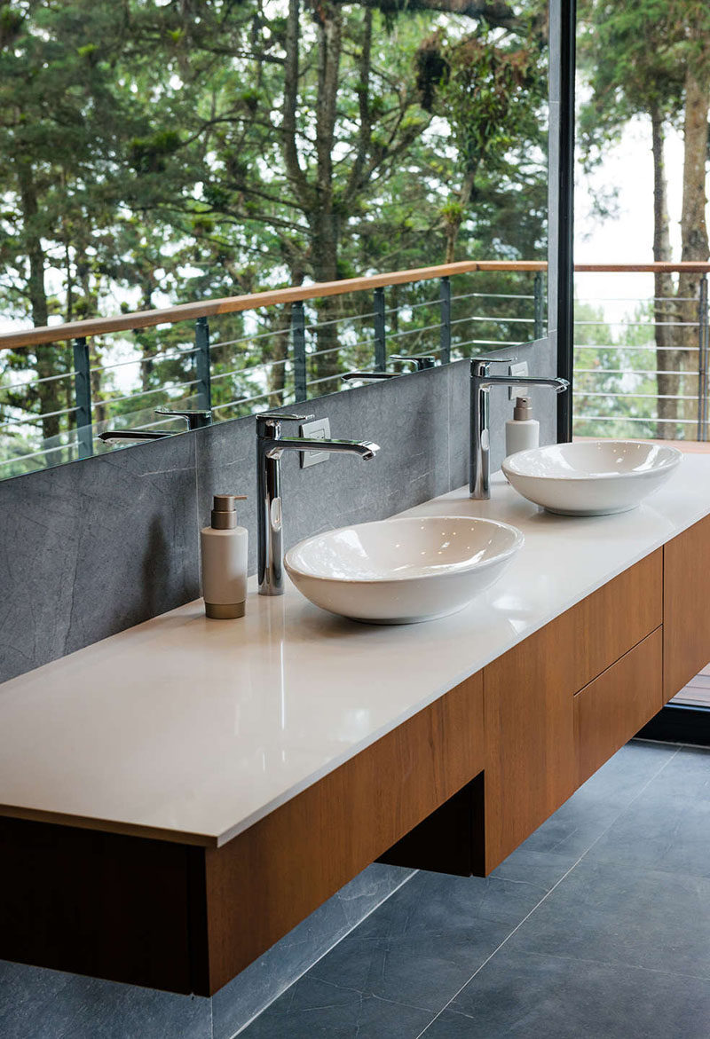 This modern bathroom has a large mirror that reflects the views from the window, and a floating wood vanity with a white countertop. #Bathroom #VanityDesign