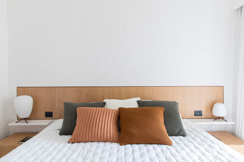 In this modern master bedroom, a wood headboard breaks up the white wall. #MasterBedroom #BedroomDesign #WoodHeadboard