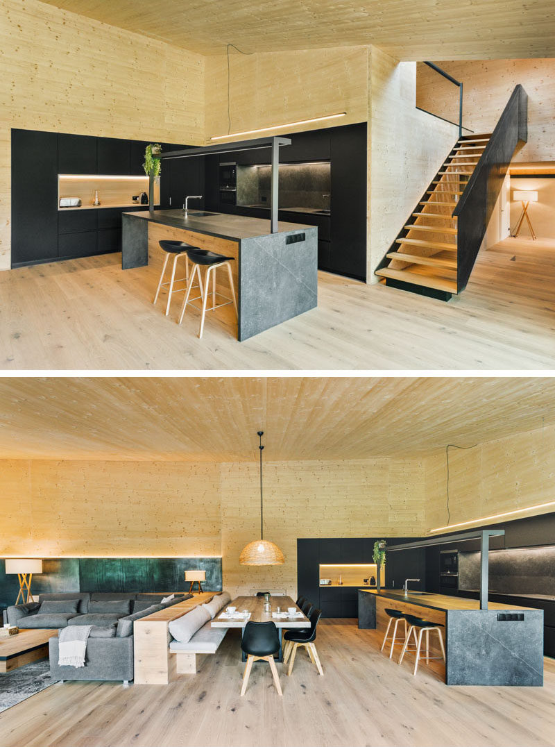 In this modern kitchen, the black cabinets complement the iron stairs, while a grey kitchen island adds a lighter touch. A pony wall separates the dining area and the living room, and provides a backrest for the bench. #BlackKitchen #PonyWall #DiningRoom #LivingRoom #OpenPlanInterior