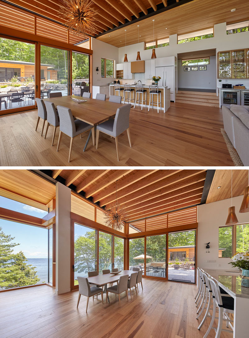 This modern cottage has large windows, an exposed ceiling, a white kitchen with an island, and a dining area that opens up to a landscaped area, creating and indoor/outdoor living environment. #CottageInterior #ModernInteriorDesign #Windows #WhiteKitchen #DiningRoom