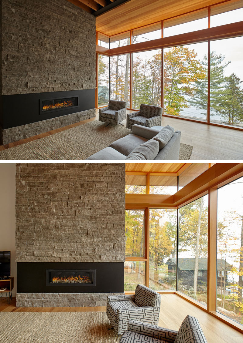 This contemporary cottage has large windows, a stone accent wall, a fireplace with a black surround, and a wood ceiling. #Cottage #Windows #WoodCeiling #Fireplace