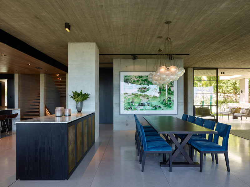 In this modern house, a pair of chandeliers hang above the large dining table, while a sideboard provides separation from the kitchen. #DiningRoom #ModernInterior