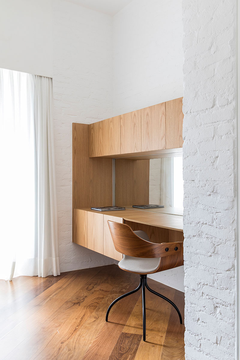 This modern master bedroom suite has a home office/vanity built into a small alcove. A mirror helps to reflect the light from the window, while the wood cabinetry provides plenty of storage. #HomeOffice #Vanity #InteriorDesign