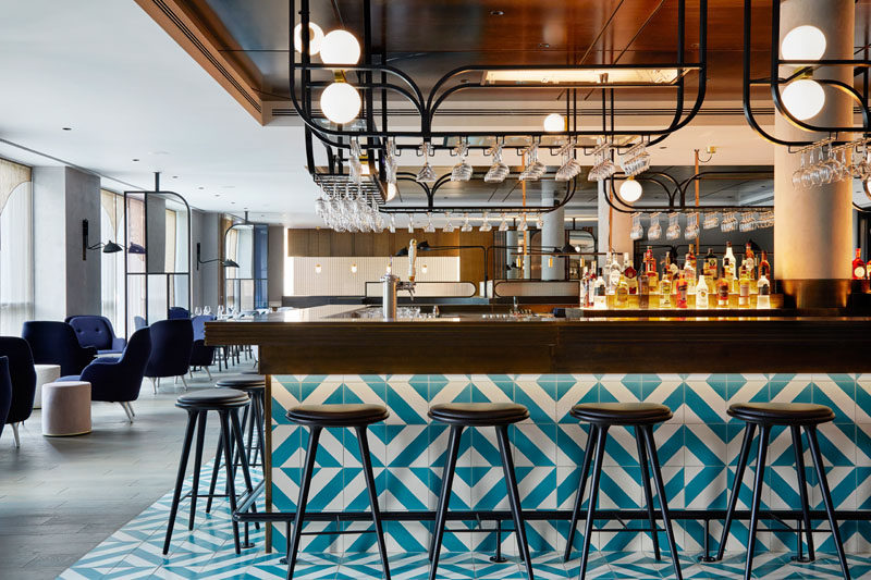 This modern hotel has a bar/restaurant with a blue and white patterned tiled bar, while hanging black racks provide a place to store glassware. #HotelBar #BarDesign