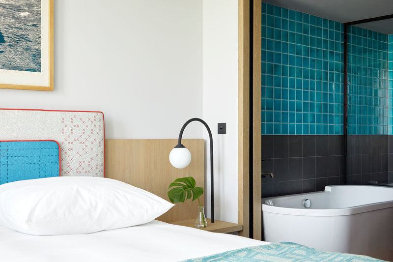 In this modern hotel room, simple furnishings have been paired with a bathroom that adds a pop of color with the use of bright blue tiles. #HotelRoom #BlueTiles #ModernBathroom