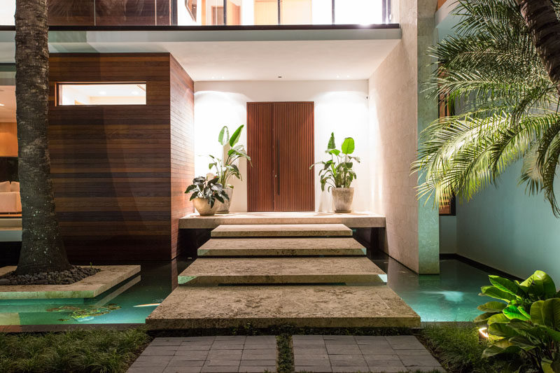 Upon arriving at this modern house, there's a small bridge to cross above the reflecting ponds, before reaching the wood front door. #Bridge #Landscaping #WaterFeature #WoodFrontDoor