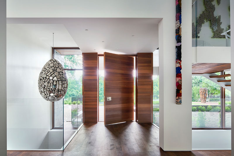 A large pivoting wood doors greets people as they arrive to this modern house, and is immediately apparent that the home is filled with art pieces. #WoodFrontDoor #PivotDoor #PivotingFrontDoor