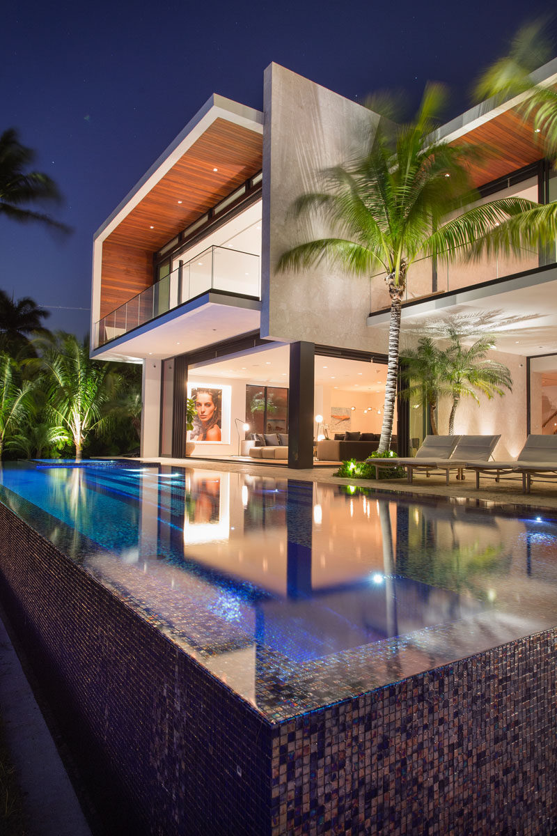 An infinity-edge pool in the backyard of this modern house is surrounded by limestone decking, which contrasts the iridescent blue tile used in the pool and spa. #SwimmingPool #ModernHouse #LimestoneDecking