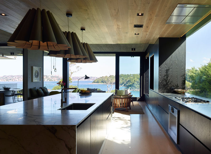 In this modern kitchen, dark wood cabinetry contrasts the light floor and ceiling, while a large picture window provides ample natural light. #KitchenDesign #ModernKitchen