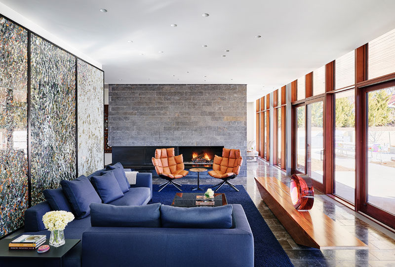 In this modern living room, large artwork becomes the backdrop for the blue couch, while floor-to-ceiling windows provide ample natural light. #ModernLivingRoom #LivingRoomLayout