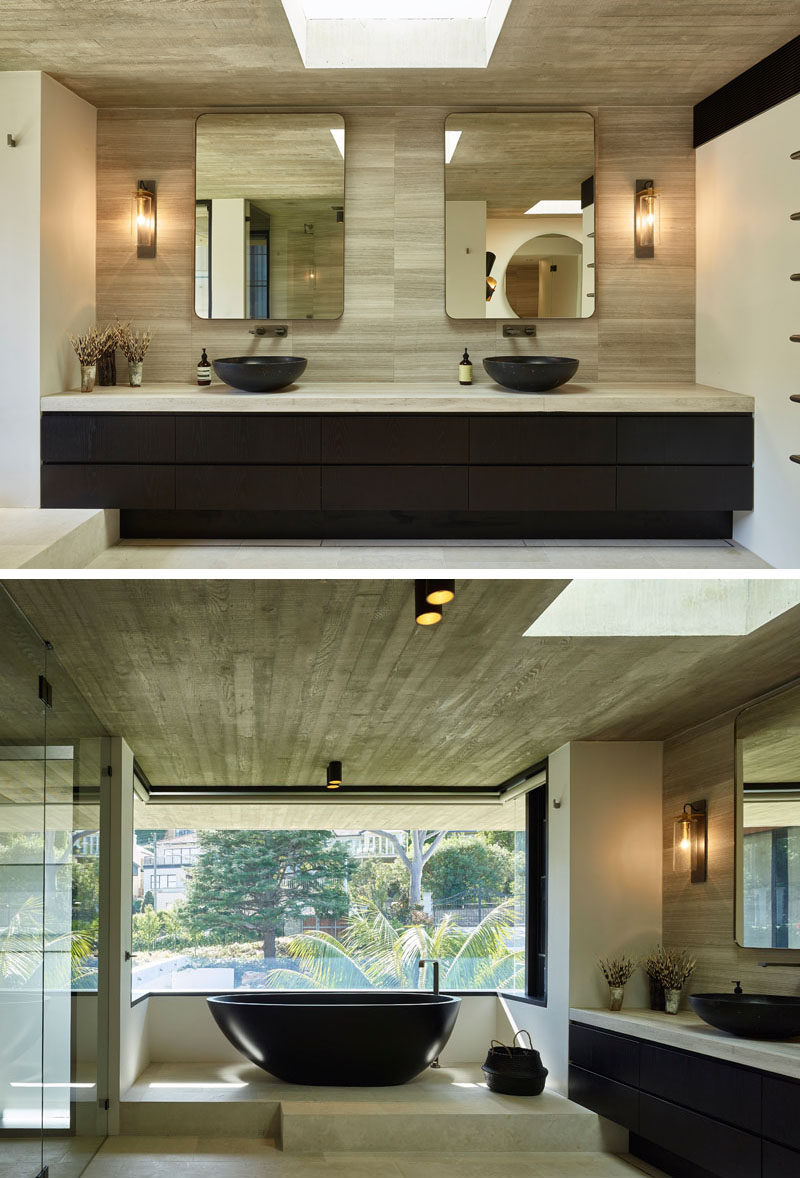 In this modern master bathroom, there's a dual sink vanity that runs the length of the wall, while a freestanding bathtub is raised up onto a platform to take advantage of the views. Blinds can be lowered when privacy is needed. #MasterBathroom #BathroomDesign