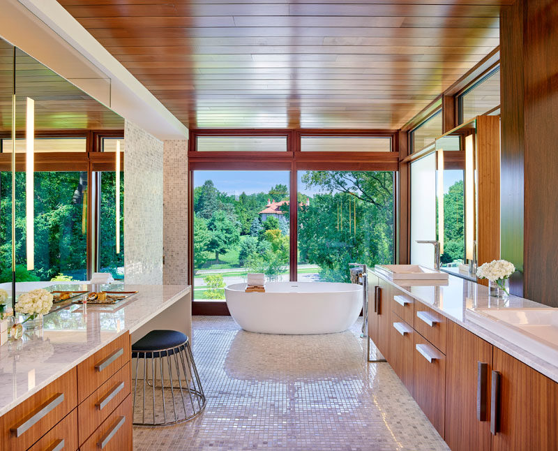 In this master bathroom, there's a freestanding bathtub that's positioned in front of the window, a double sink vanity, and a second vanity area with space for a stool. #MasterBathroom #BathroomDesign #EnsuiteBathroom