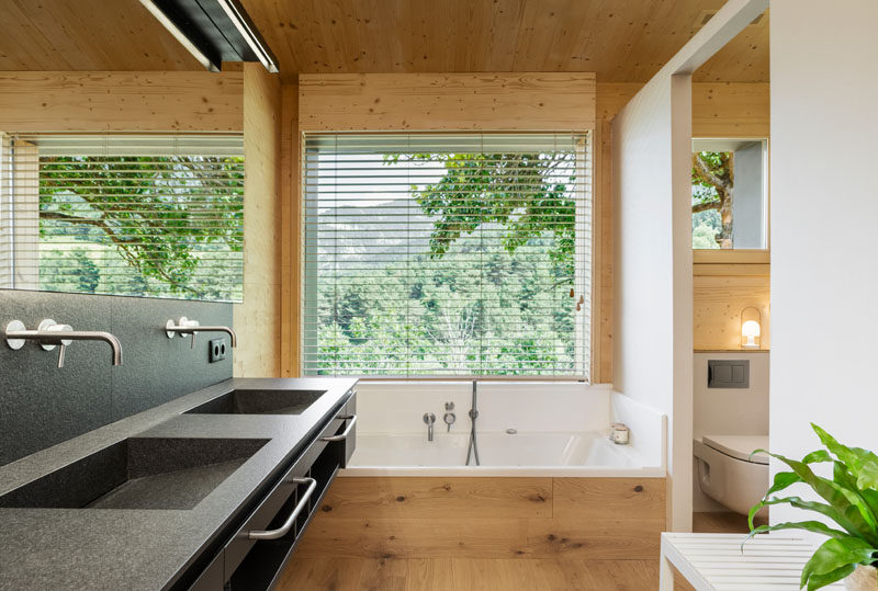 In this modern master bathroom, there's a built-in bathtub located below a window, while behind a partial wall is the toilet and shower. #ModernBathroom #BuiltInBathtub