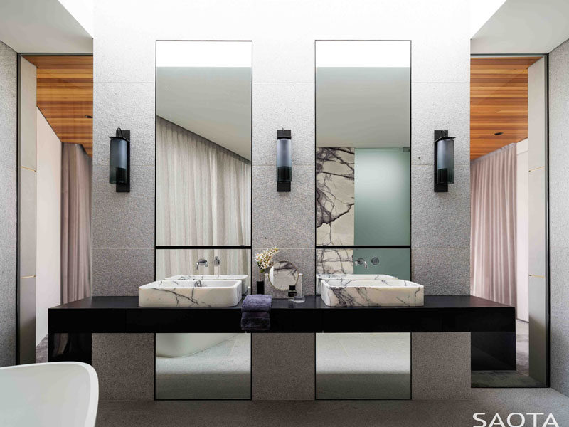 In this modern master bathroom, there's a black vanity topped with stone basins, while two tall mirrors reflect the light within the room. #MasterBathroom #EnsuiteBathroom