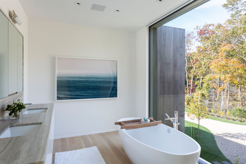 In this modern master bathroom, a freestanding bathtub is positioned in front of the large window, that adds plenty of natural light to the room. #ModernBathroom #BathroomDesign