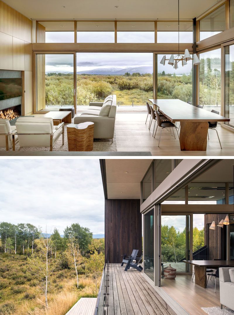 The open plan living room and dining room of this modern house, has sliding glass doors that open to a wrap-around balcony with expansive views of the landscape and mountains beyond. #ModernLivingRoom #ModernDiningRoom #SlidingGlassDoors #Balcony