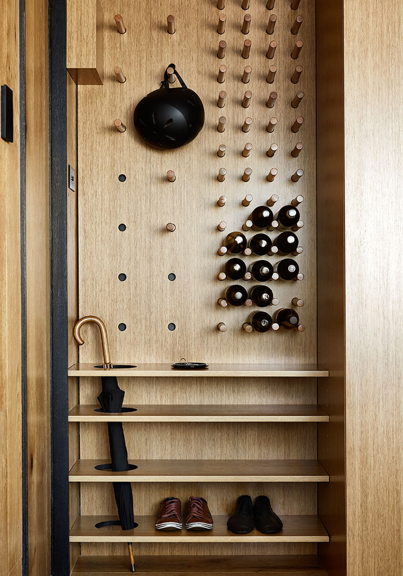 Upon entering this modern and small apartment, there's a custom designed wall unit that features a flexible pegboard wall, creating a place to hang jackets, keep umbrellas and store shoes. The other half of the pegboard wall has fixed dowels to create wine storage. #Entryway #Storage #ShoeStorage #UmbrellaStand #WineStorage