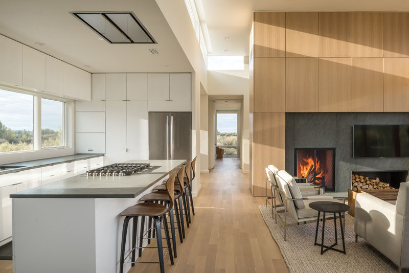 The top floor of this modern house is home to a mostly white kitchen with minimalist cabinets, and an open plan living and dining room. #Fireplace #WhiteKitchen #WoodFloors