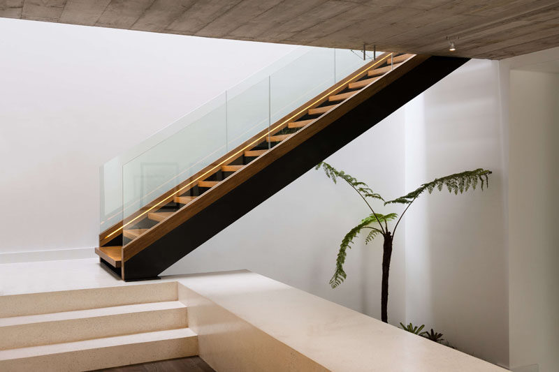 Wood and steel stairs with a glass handrail, located by the front door of this modern house, lead up to the bedrooms. #Stairs #ModernStairs