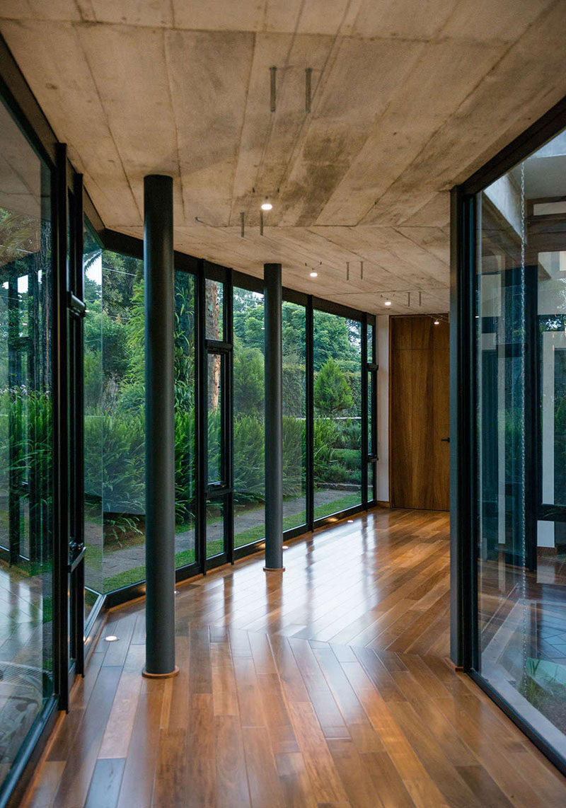 This modern house has hallways with walls of windows, a concrete ceiling, and wood floors. #Hallway #Windows