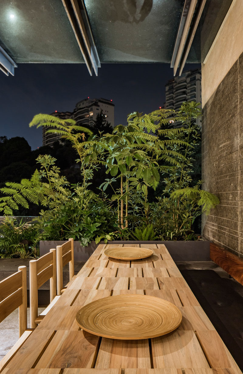 This covered balcony has a dining area with a long wood table and planters filled with lush plants. #OutdoorDining #Balcony #Planters