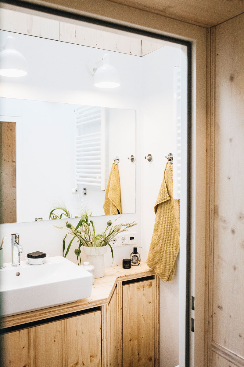 The bathroom in this tiny home has a walk-in rain shower, and natural light from the skylight is reflected in the small room by the mirror, helping to keep it bright. #TinyBathroom #TinyHome