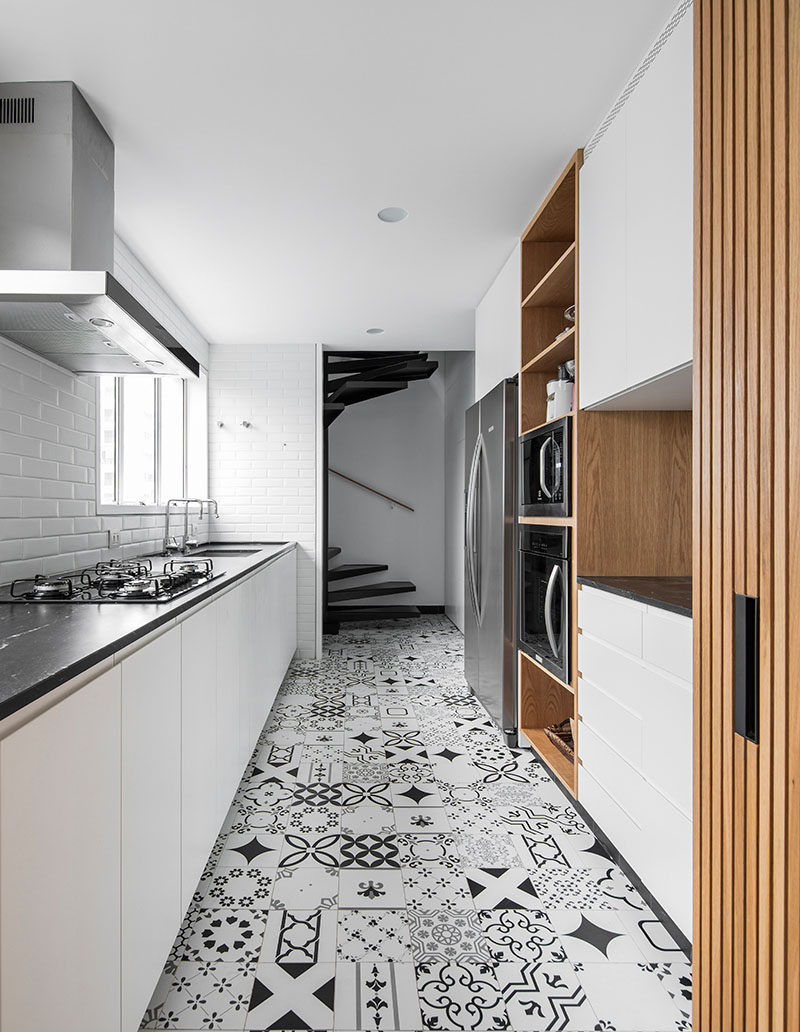 In this modern kitchen, white cabinets have been paired with wood elements, a dark countertop, and patterned floor tiles. #ModernKitchen #PatternedFloorTiles #WhiteKitchen