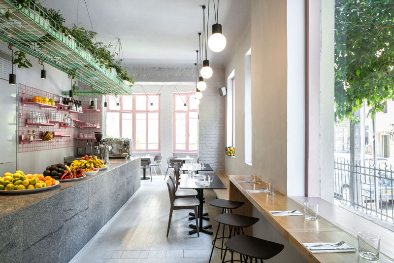 Amit Design Studio has recently completed Bana, an organic food cafe that's located in Tel Aviv, Israel, and has design features like pink metal grid shelving and a large basket filled with plants that hangs from the ceiling. #CafeDesign #ModernCafe #InteriorDesign