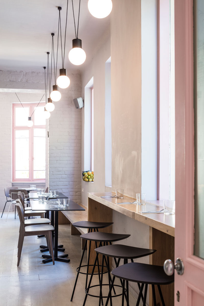 A bar height counter is positioned in front of the windows of this modern cafe, while the wood counter continues to become a bench for table seating. #ModernCafeSeating #CafeDesign #InteriorDesign