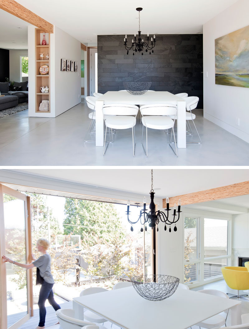 In this dining room, a square white dining table sits below a black chandelier, while an eight foot high scenic door folds away to open the interior to the backyard. #ModernDiningRoom #FoldableDoors