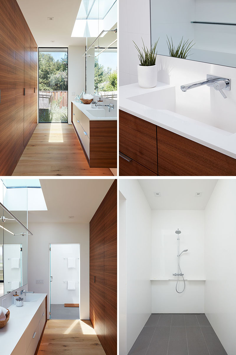 In this modern master bathroom, a wood accent wall hides the door and reflects the wood of the vanity, while the mirror reflects the natural light from the skylight and window. In the shower, grey tiles contrast the white walls and ceiling. #MasterBathroom #BathroomDesign