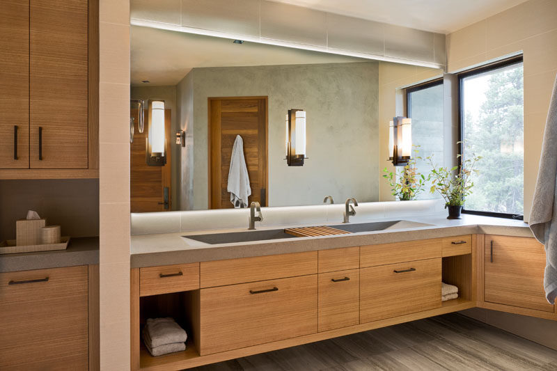 In this modern guest bathroom, a floating wood vanity is topped with a custom concrete countertop, while a large backlit mirror reflects light throughout the room. #ModernBathroom #ConcreteCounter #WoodVanity