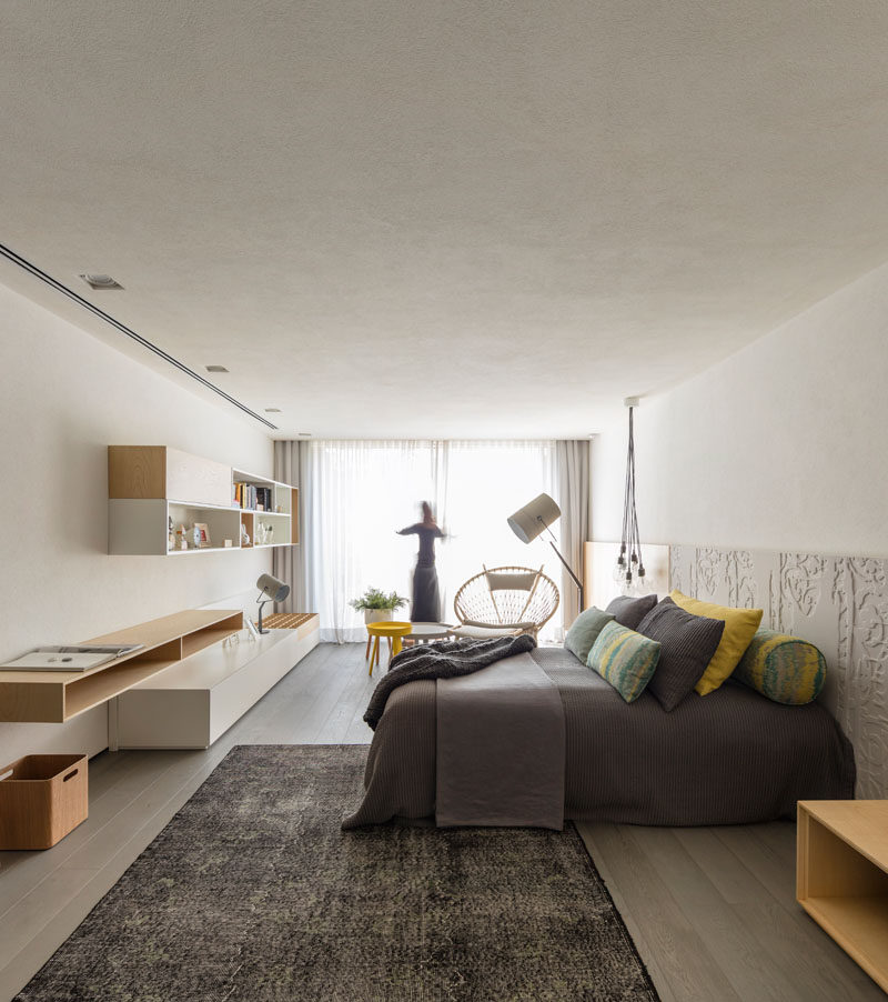 In this modern guest bedroom, large windows provide ample natural light to the small sitting area and the rest of the room, while a patterned headboard becomes a backdrop for the bed. #ModernBedroom #BedroomDesign