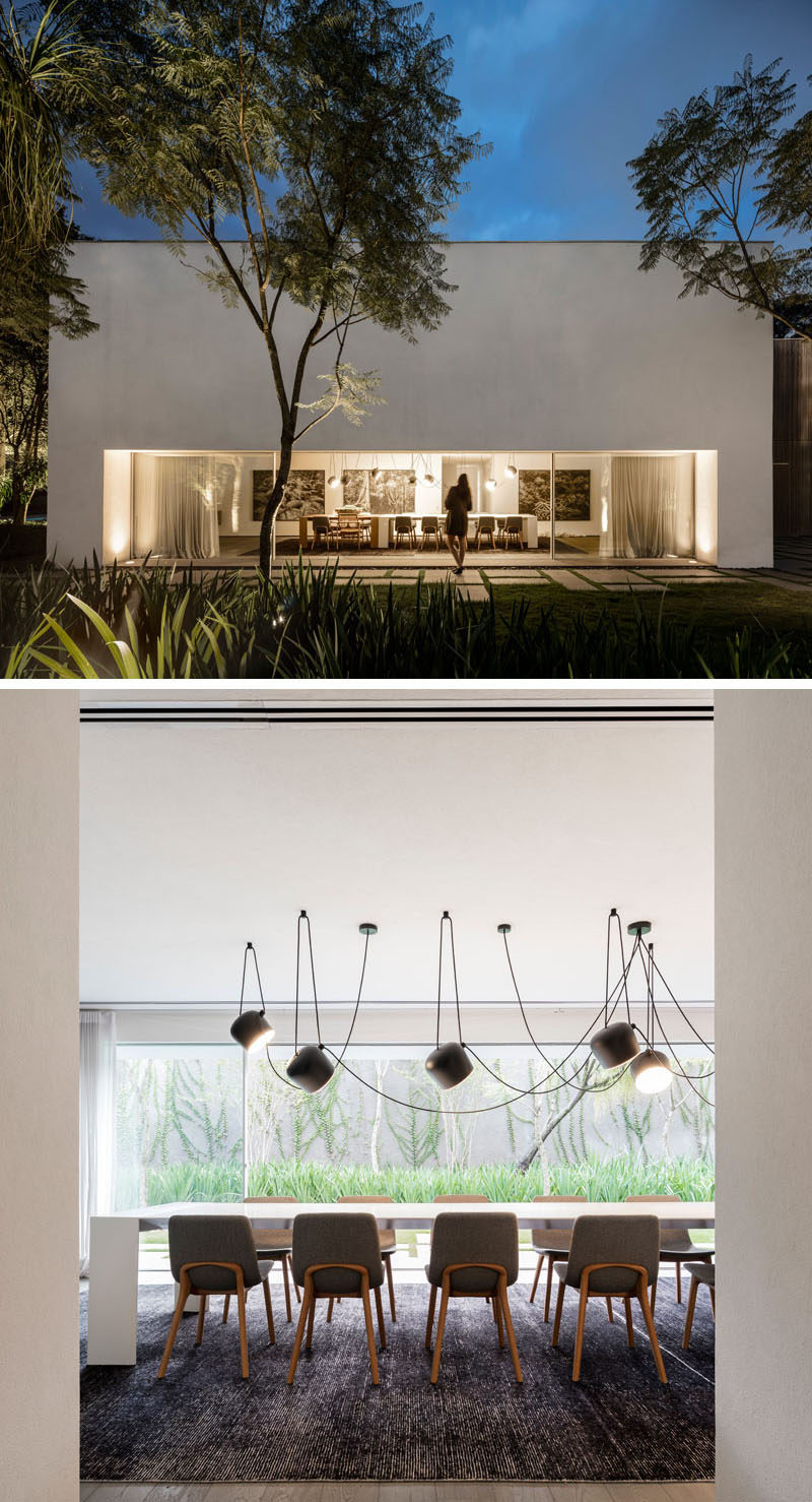 In this modern dining room, a long table makes sure there's plenty of room for guests, while artwork breaks up the mostly white interior. #ModernDiningRoom #GlassWall