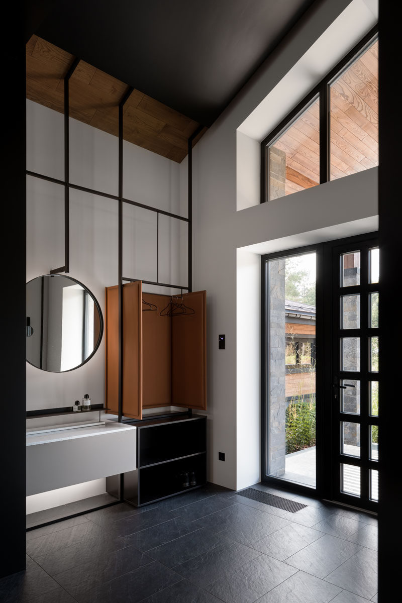 Stepping inside this modern house, the high ceilings throughout the home are immediately apparent. A custom designed multi-purpose furniture piece in the entryway provides a place to hang jackets and store shoes. #Entryway #ModernInteriorDesign #HighCeilings