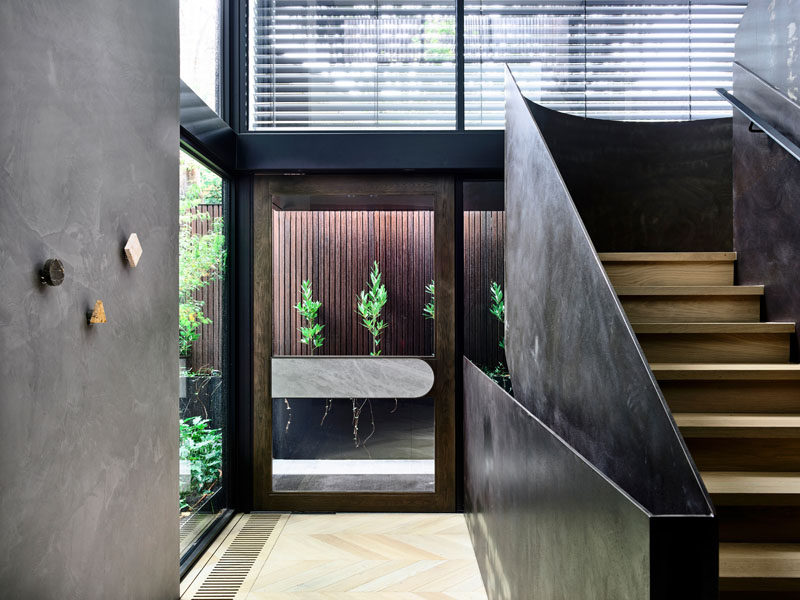 A glass front door welcomes visitors to this modern house, and once inside the double height ceilings and windows allow the entryway to be bright and open. #ModernFrontDoor #GlassFrontDoor #SteelStairs