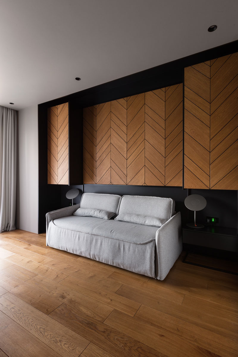 In this home office / guest suite, there's a wood accent wall with a chevron pattern. A couch sits between two side tables, and when required for guests, can be transformed into a bed. #HomeOffice #GuestSuite #ChevronAccentWall