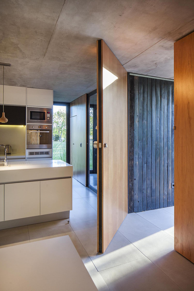 A large wood front door located next to the blackened wood exterior accent welcomes visitors to this modern house. #WoodFrontDoor #ModernHouse