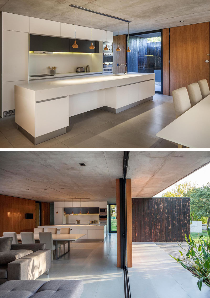 This modern kitchen features a large white island and minimalist white cabinets. Simple turned wood pendant lights hang above the island. #WhiteKitchen #KitchenDesign #WhiteIsland