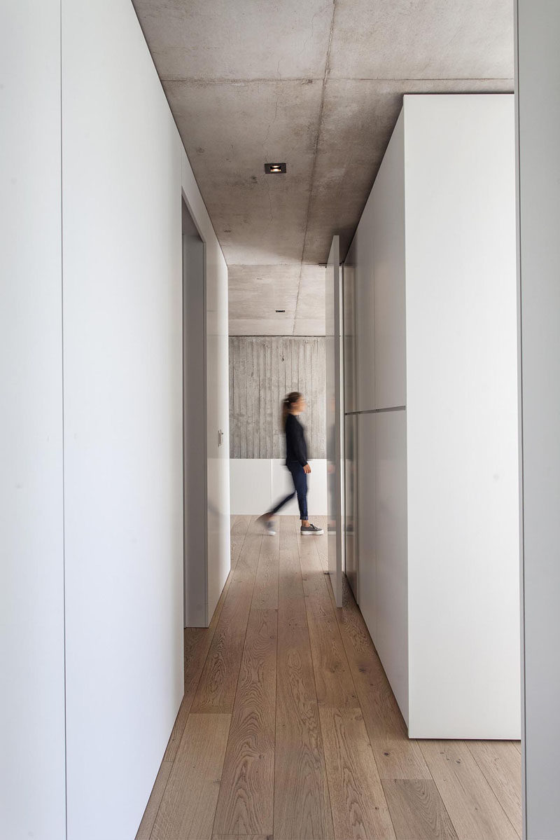 Raw concrete contrasts the bright white walls and cabinets that line the hallway in this modern house, while wood flooring adds warmth and a natural touch. #ConcreteCeiling #WoodFlooring #WhiteHallway